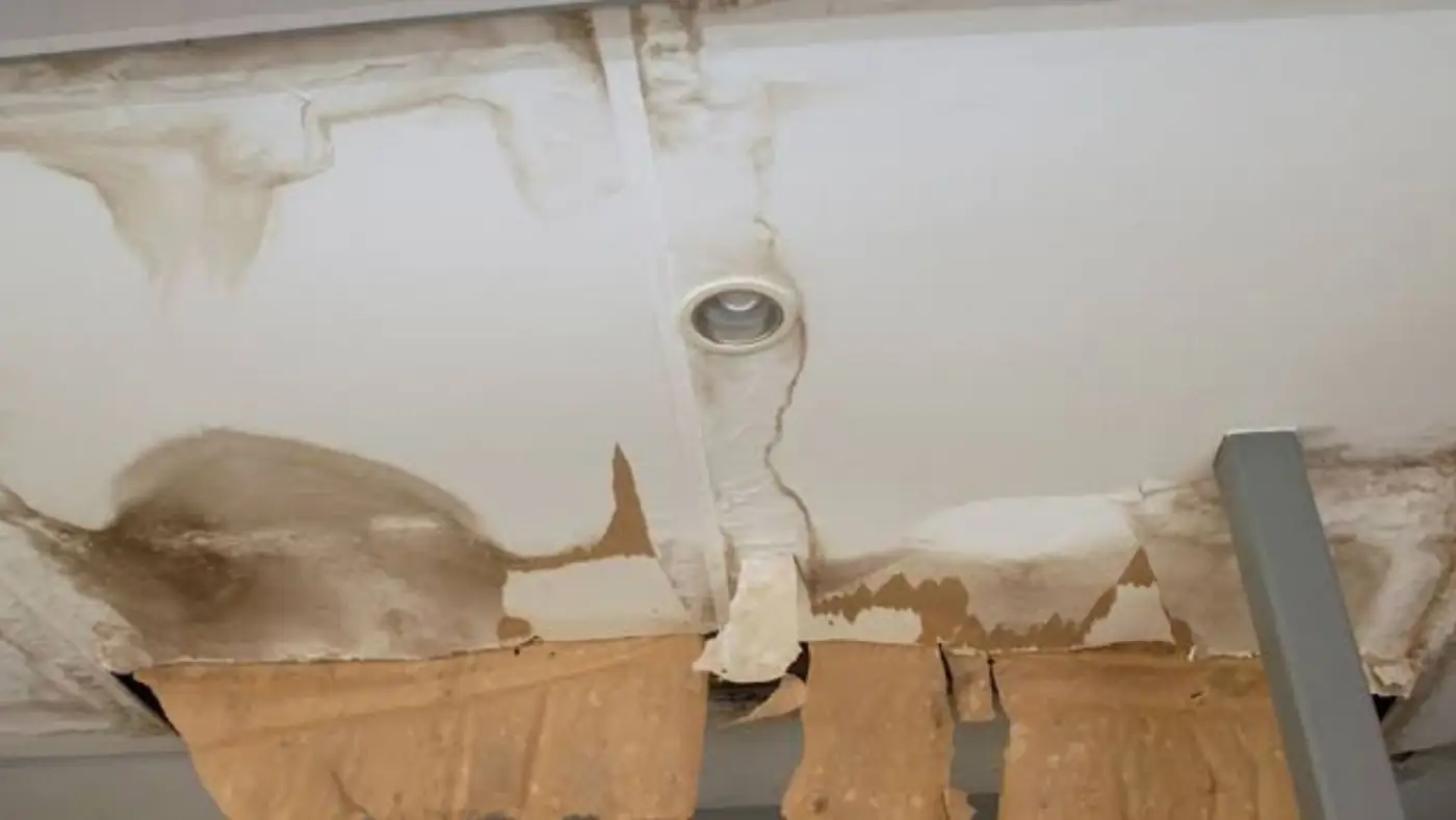 Ceiling with a stained, peeling section around a pipe fitting after a leak