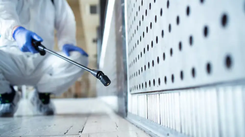 Technician in protective gear treating a surface near floor level